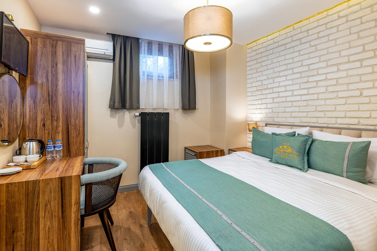 A hotel room with a bed, a desk with a chair, a wardrobe, and a window with curtains.