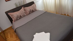 A neatly made bed with a grey bedspread and two decorative pillows, a wooden floor, and a window with sheer curtains. - Victoriei 7 - 2 bedroom apartment downtown (Sector 1)
