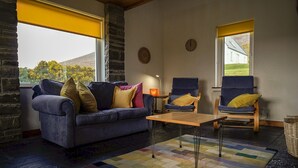 Ein gemütliches Wohnzimmer mit einer Couch, zwei Sesseln, einem Couchtisch und Blick ins Freie.