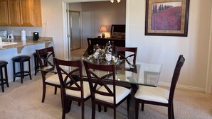 A dining area with a glass table, wooden chairs, and a chandelier. - Greenview Getaway by Mesquite Vacation Rentals at Wolf Creek Golf Course Condo with $510 in free daily activities (Mesquite)
