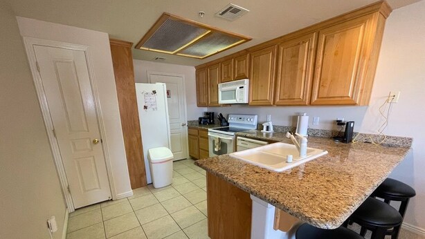 A kitchen with granite countertops, wooden cabinets, a microwave, a stove, and a sink. - Greenview Getaway by Mesquite Vacation Rentals at Wolf Creek Golf Course Condo with $510 in free daily activities (Mesquite)