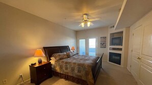 A bedroom with a bed, nightstand, lamp, ceiling fan, TV, and a door. - Greenview Getaway by Mesquite Vacation Rentals at Wolf Creek Golf Course Condo with $510 in free daily activities (Mesquite)