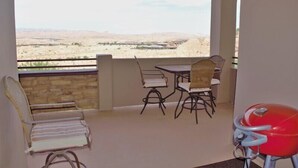 A balcony with a view of a desert landscape, a red barbecue grill, and a table with chairs. - Greenview Getaway by Mesquite Vacation Rentals at Wolf Creek Golf Course Condo with $510 in free daily activities (Mesquite)