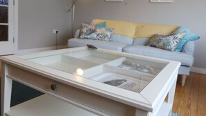 Una sala de estar moderna con una mesa de centro de vidrio, un sofá de color claro con cojines estampados y una lámpara de pie.