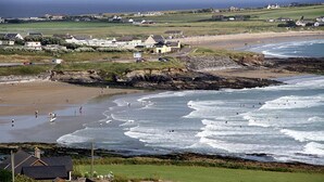 A coastal beach with waves, a sandy shore, and houses in the background. - Kinsale No 6 (Kinsale)
