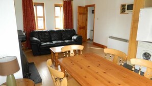 A dining area with a wooden table and chairs, a black leather sofa, and a kitchen area with a washing machine. - Kinsale No 6 (Kinsale)