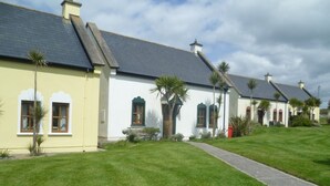 A row of white buildings with dark roofs, green window frames, and a well-maintained lawn. - Kinsale No 6 (Kinsale)