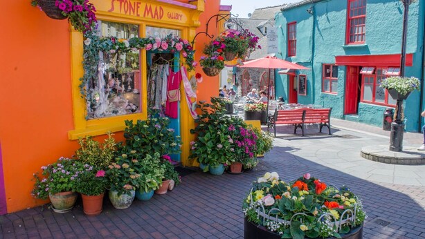 A colorful storefront with a sign reading "STONE MAD GALLERY," surrounded by potted plants and outdoor seating. - Kinsale No 6 (Kinsale)