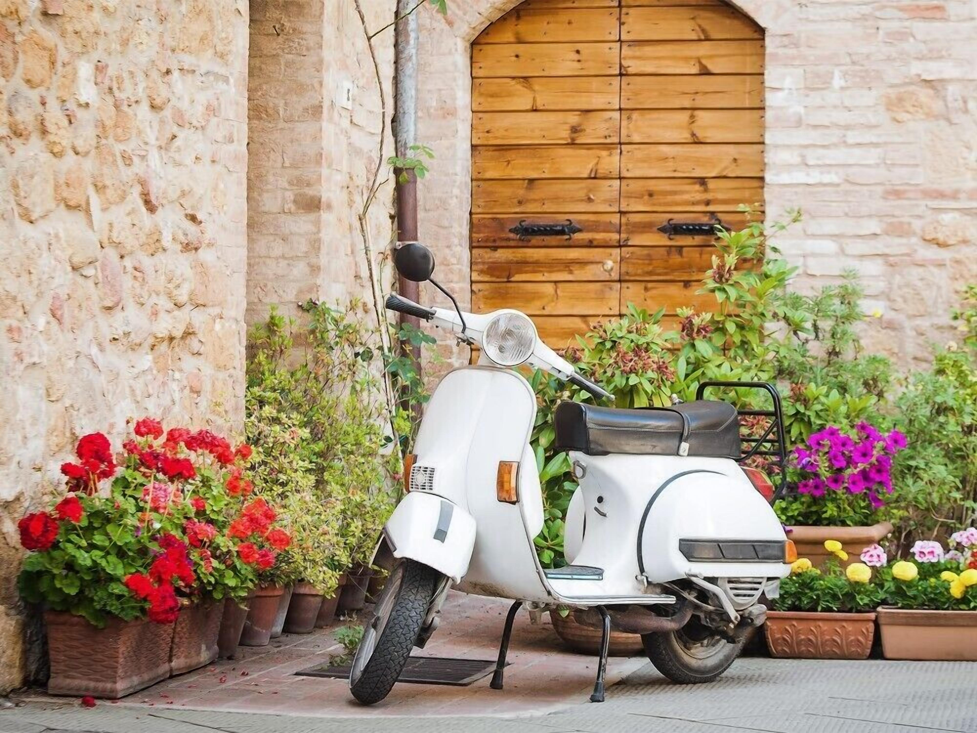 A white scooter parked in front of a stone building with a wooden door.