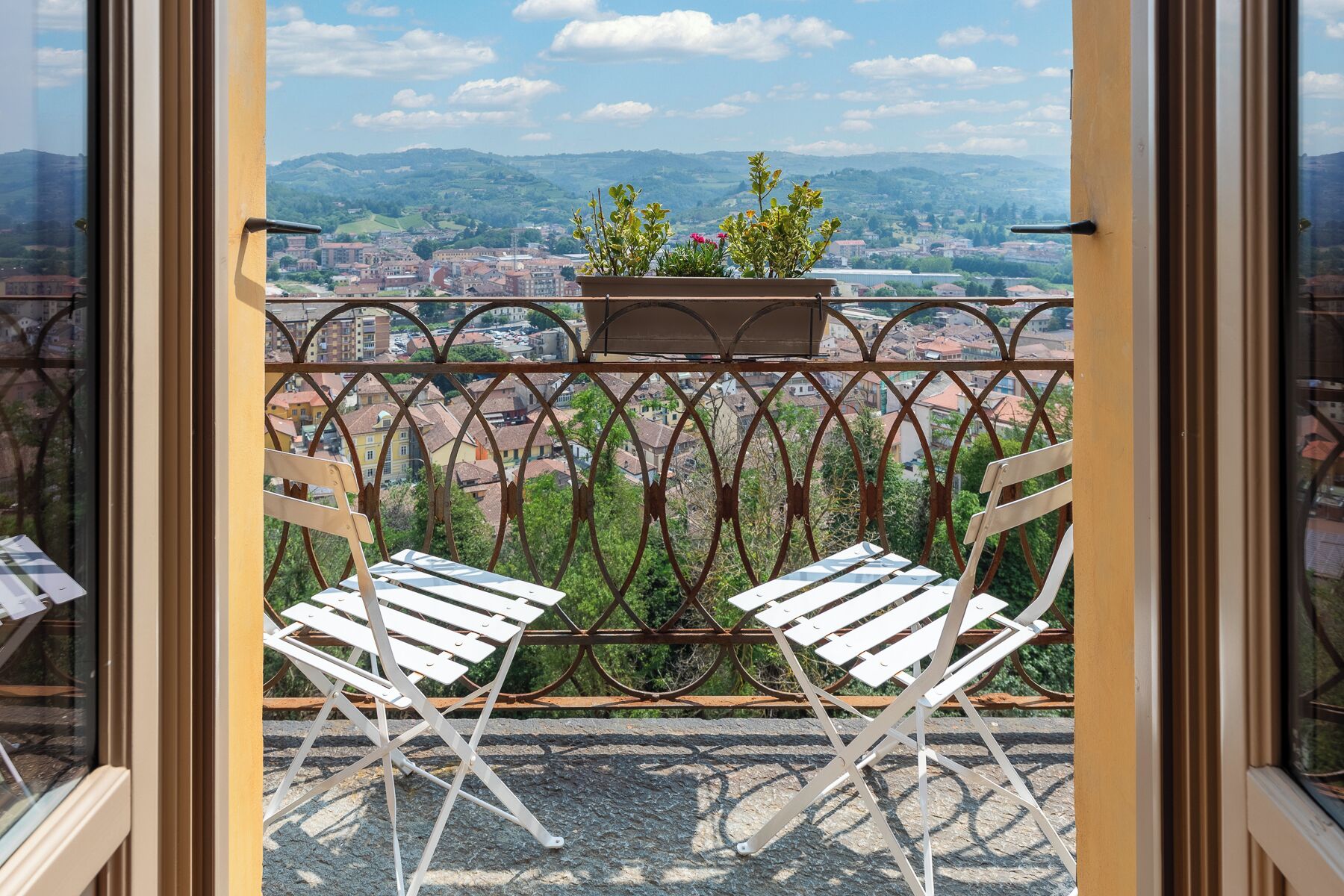 A balcony with two white chairs, a metal railing, and a potted plant.
