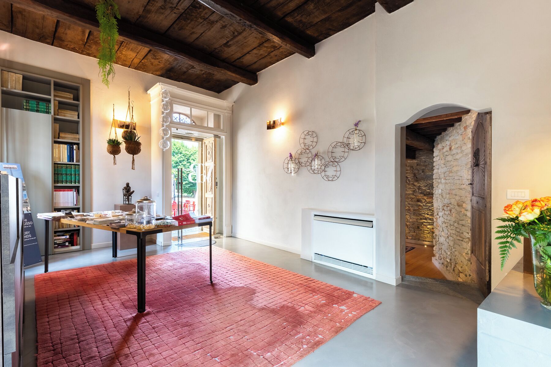 A spacious room with a red carpet, a wooden ceiling, a stone wall, and a white radiator.