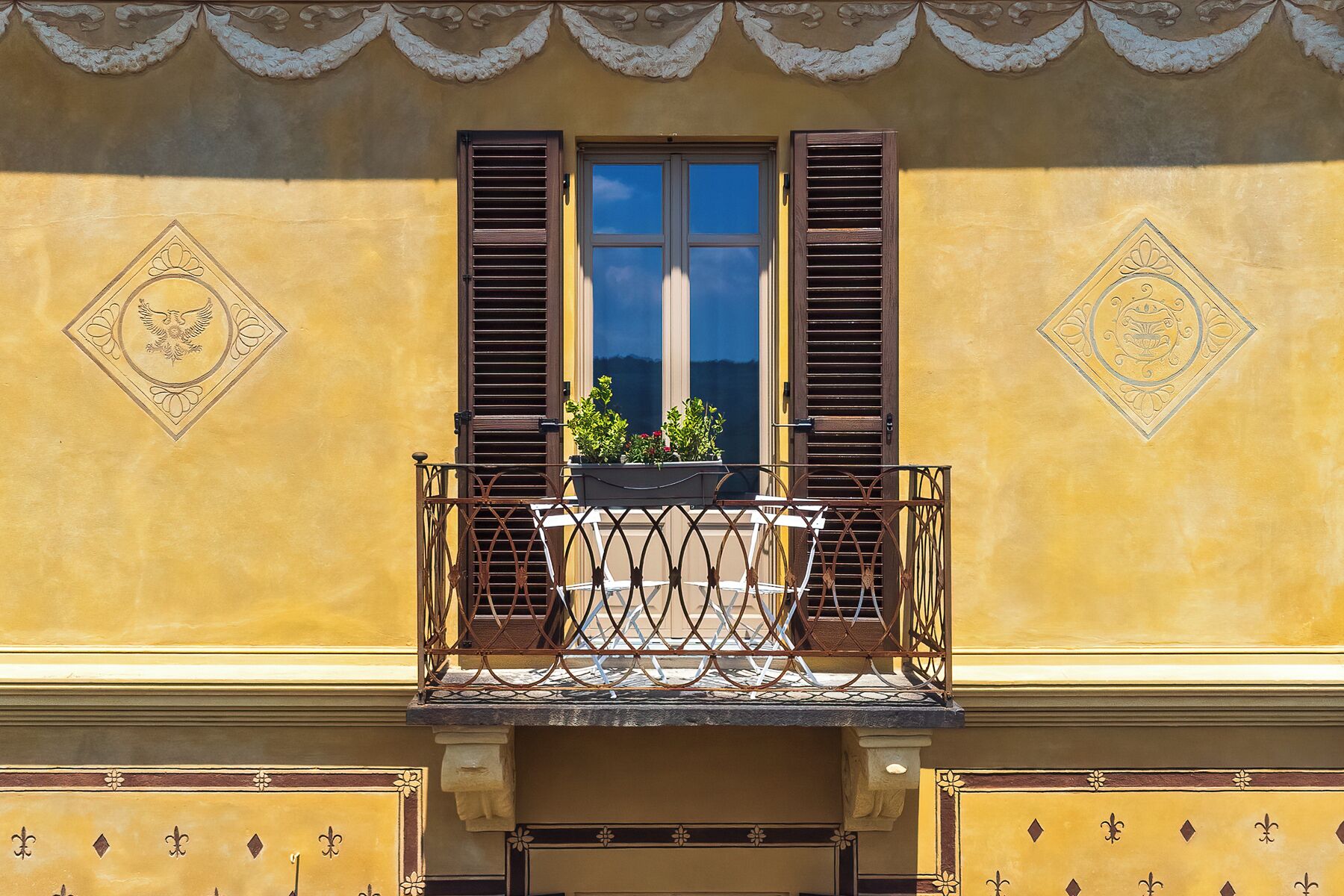 A balcony with a wrought iron railing, a window with shutters, and decorative wall patterns.