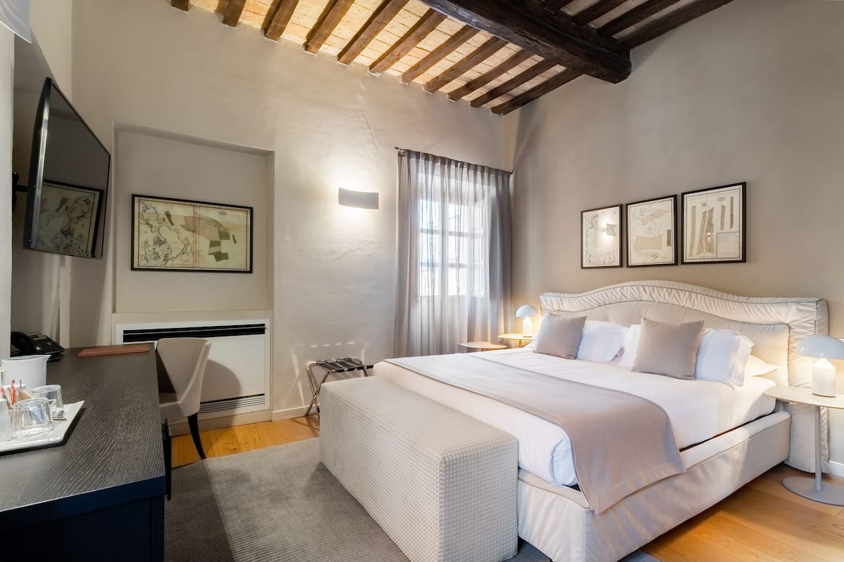 A hotel room with a large bed, a desk with a chair, a small table with a lamp, and artwork on the walls.