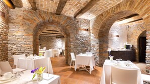 Un restaurante con paredes de piedra y techos abovedados, manteles blancos e iluminación moderna.