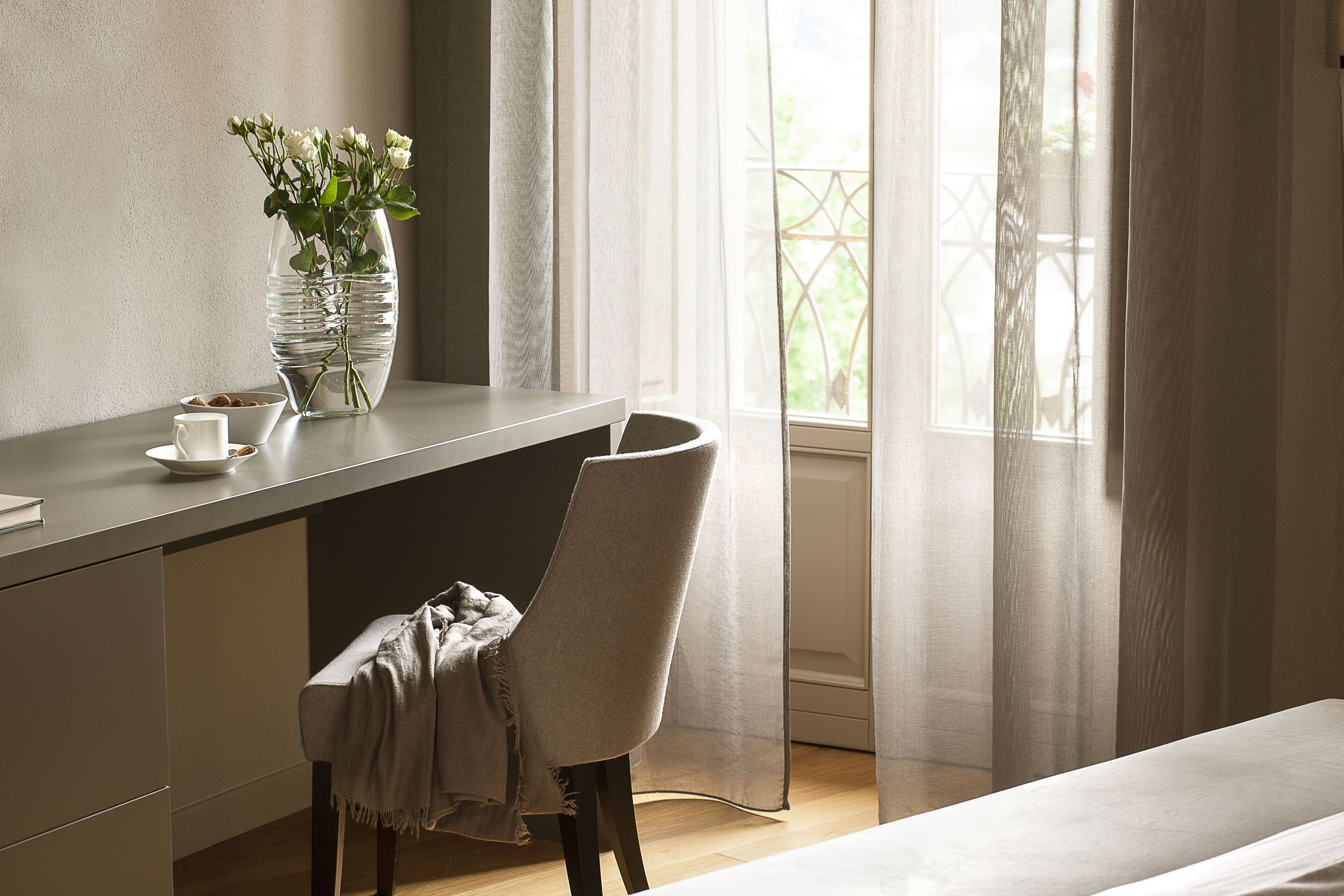Une chambre moderne équipée d’un bureau, d’une chaise et d’une fenêtre ornée de rideaux légers.