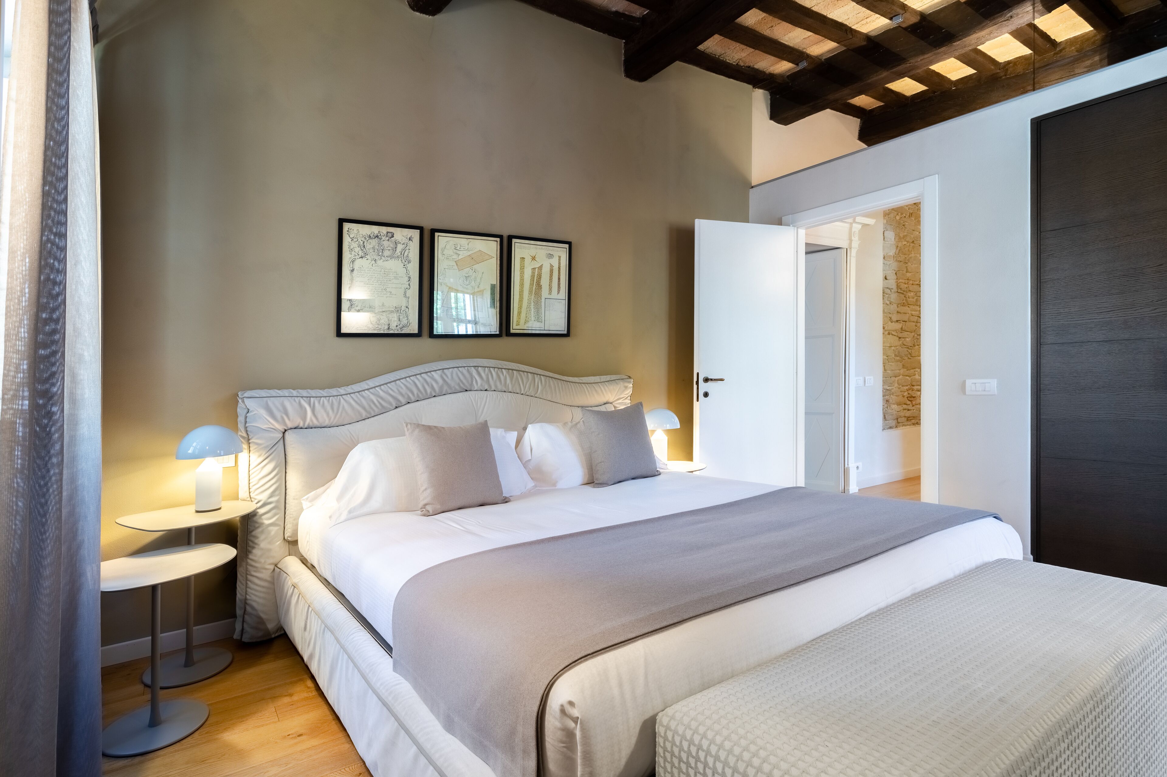 A bedroom with a large bed, two bedside tables with lamps, and a door leading to another room.