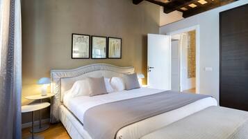 A bedroom with a large bed, two bedside tables with lamps, and a door leading to another room.