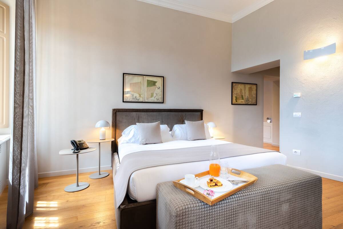A neatly made bed with white linens, a bedside table with a lamp, and a tray with breakfast items.