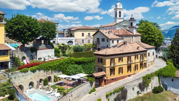 Un edificio histórico con piscina, mobiliario exterior y una iglesia al fondo.