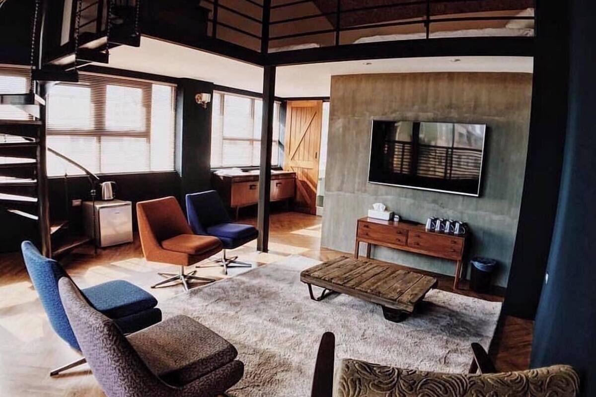 A spacious living area with a high ceiling, a large TV mounted on the wall, and a staircase leading to an upper level.