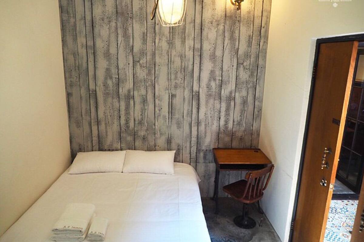 A small, neatly arranged bedroom with a bed, pillows, a desk, and a chair.