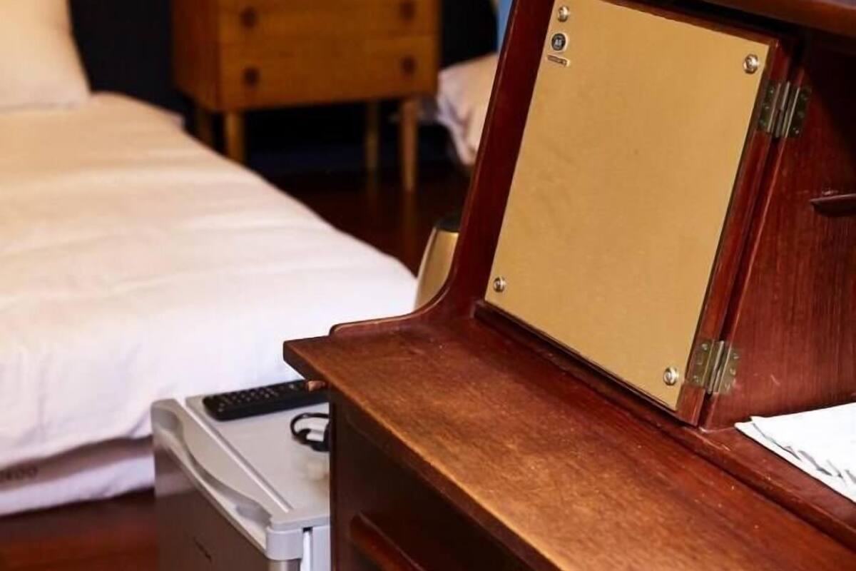 A hotel room with a wooden desk, a chair, a bed, and a nightstand with a tissue box.