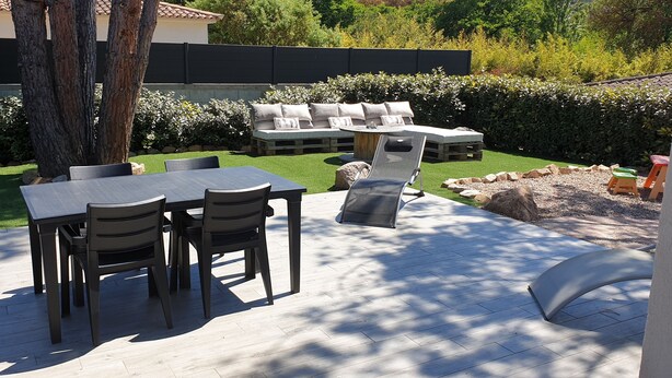 An outdoor patio with a dining table and chairs, a lounge area with cushions, and a view of a garden and building in the background. - PORTICCIO QUIET AND CLIMATE VILLA 5 MIN FROM FOOT OF AGOSTA BEACH (Albitreccia)