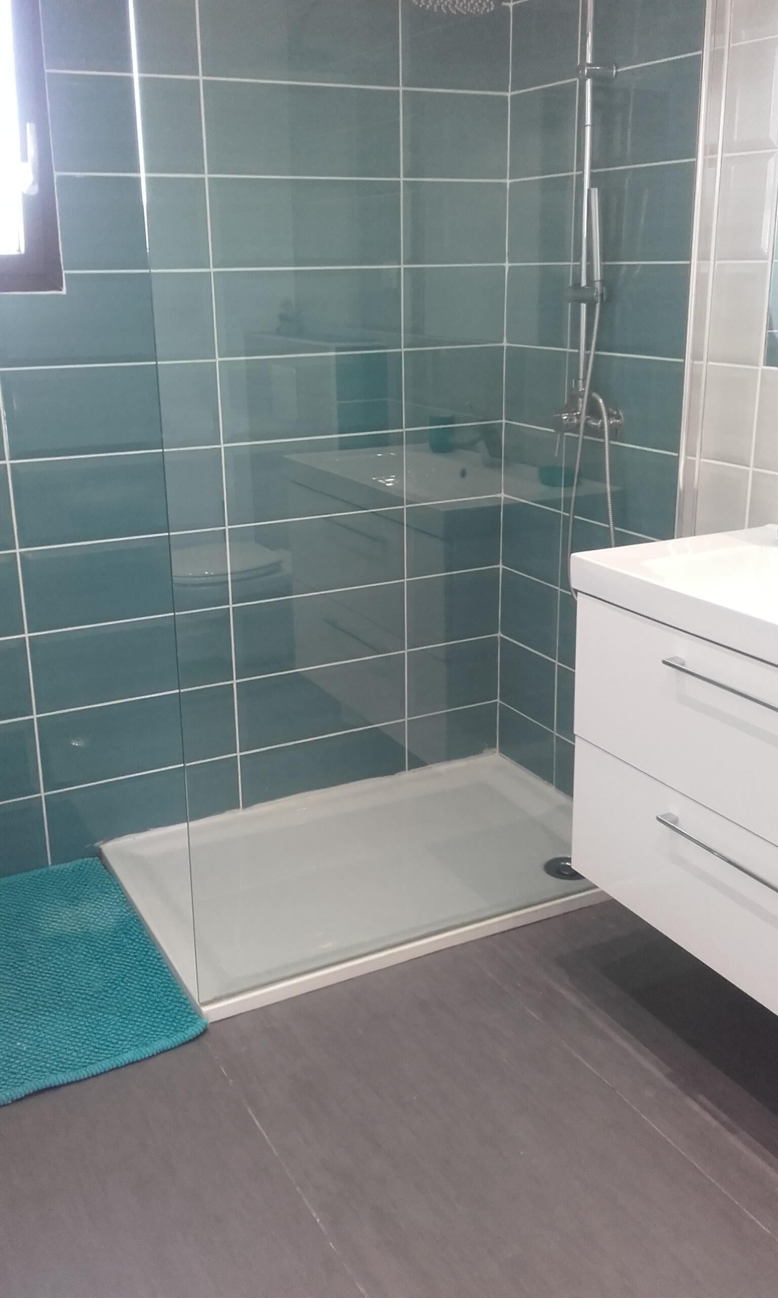 A bathroom with a glass shower enclosure, a white sink, and a teal bath mat.