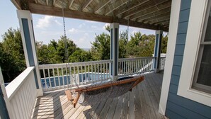 A covered porch with a hammock, wooden deck, and a view of a swimming pool.