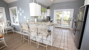 A kitchen with a central island, white cabinetry, and a dining area with wicker chairs.