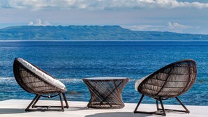 Two wicker lounge chairs with cushions facing a body of water and a mountainous landscape in the background. - Villa Gita Segara (Manggis)
