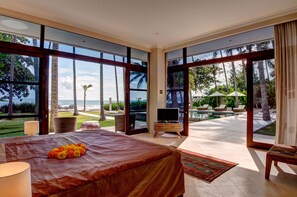 A spacious bedroom with a large bed, a TV, and a view of the ocean through large windows.