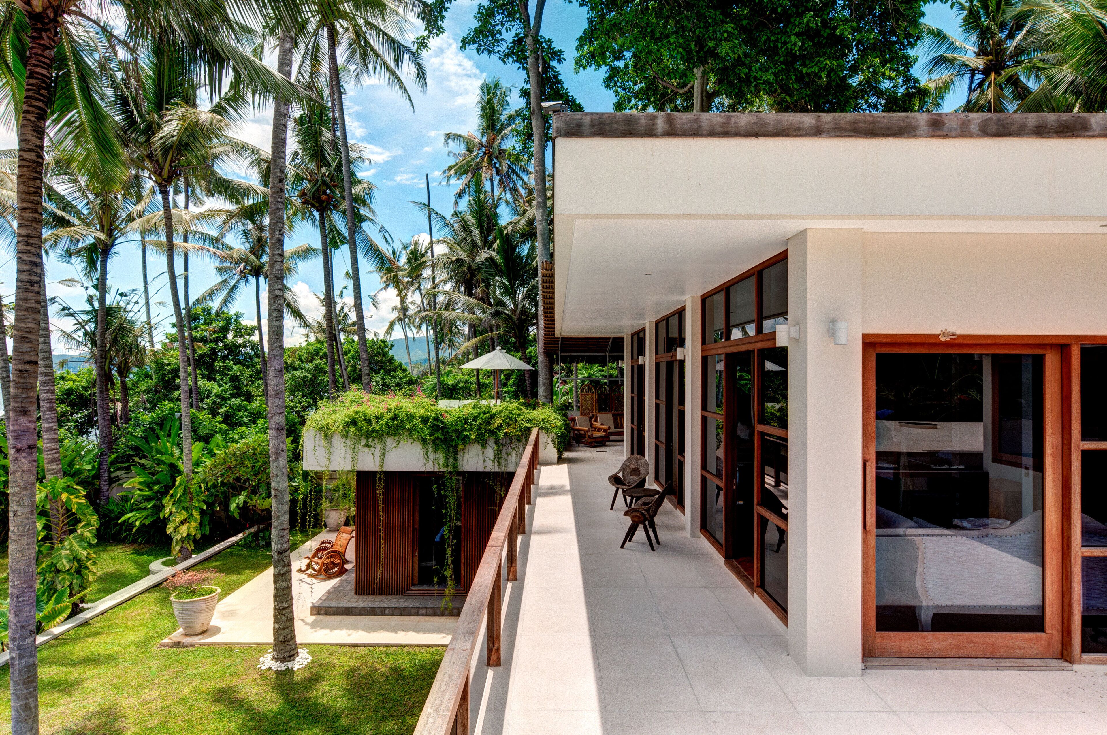 A modern house with a balcony overlooking a lush garden and palm trees.