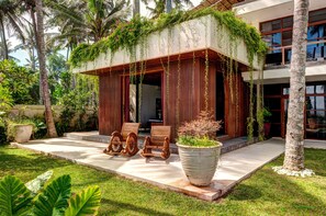 A modern building with a covered porch, wooden furniture, and lush greenery.