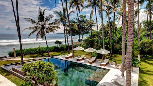 A pool with lounge chairs and umbrellas, surrounded by palm trees and a view of the ocean. - Villa Gita Segara (Manggis)