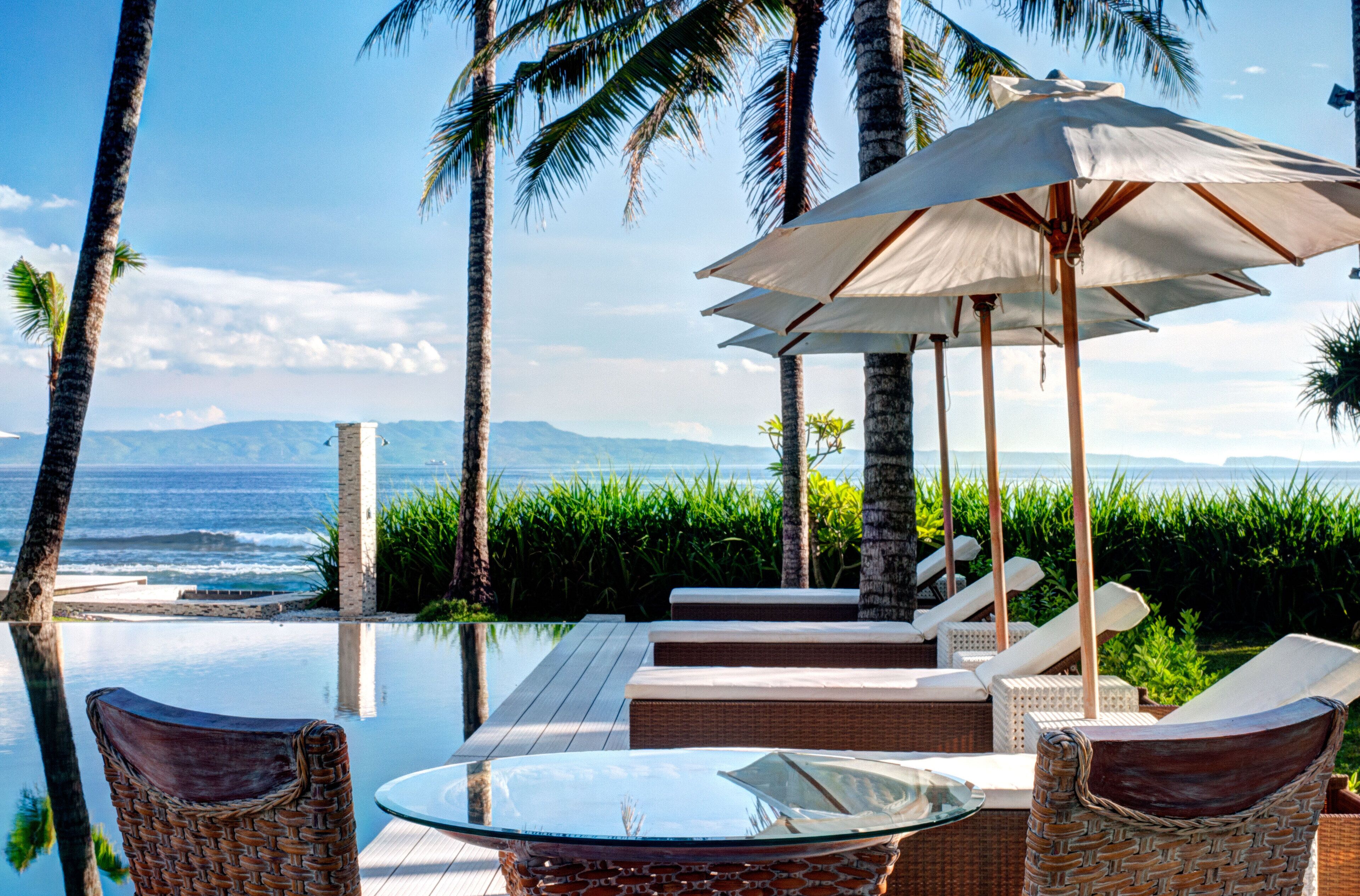 An infinity pool with lounge chairs and an umbrella, overlooking the ocean.