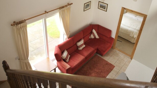 Une pièce avec un canapé rouge, un escalier en bois et une lucarne.