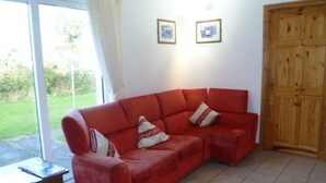 Un canapé d’angle rouge avec des coussins à motifs, une porte en bois et deux tableaux encadrés accrochés au mur.