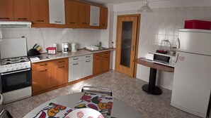 Een keuken met houten kastjes, een fornuis, een magnetron en een tafel met een kleurrijke tafelkleed.