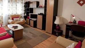 Een woonkamer met een bank, een salontafel, een televisie, een lamp en een bureau met een stoel.