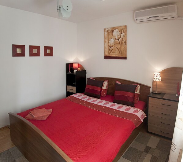 Une chambre à coucher comprenant un lit, des tables de chevet, un climatiseur fixé au mur et un tableau.