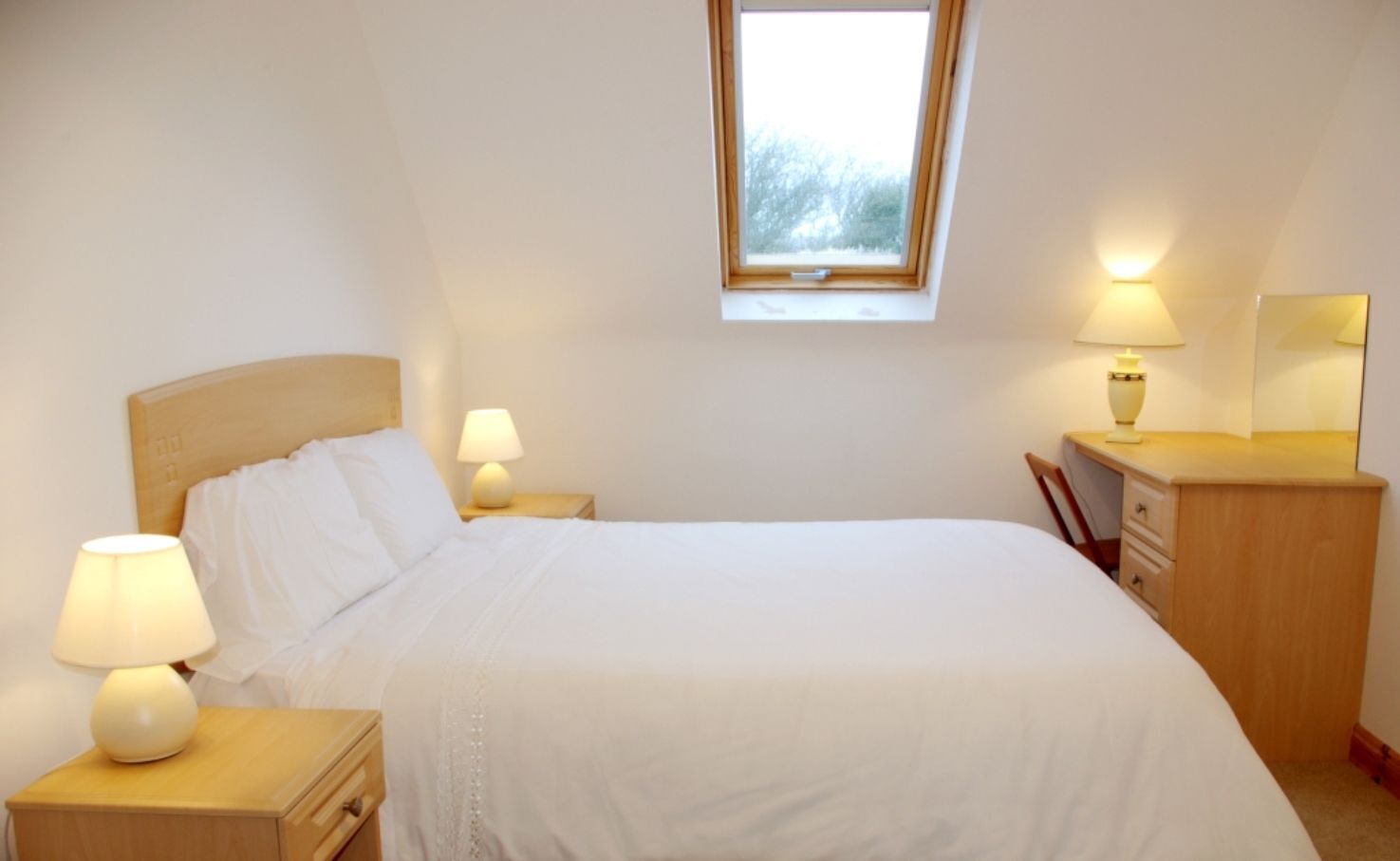 A neatly arranged bedroom with a bed, bedside lamps, a nightstand, a dresser, and a window.