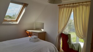 Un dormitorio con cama, un escritorio con silla, un ventanal con cortinas y vistas al exterior.