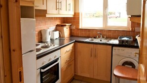 Una cocina compacta con armarios de madera, horno integrado, lavadora y ventana con un canasto rojo y blanco.