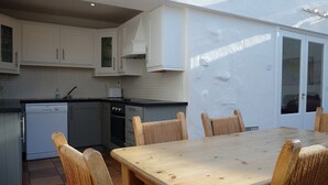 A kitchen with white cabinets, a dishwasher, an oven, and a dining table with chairs. - Ballyvaughan Cottage No 4 (Ballyvaughan)