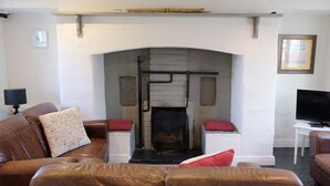 A living room with a fireplace, leather sofas, a television, and a white wall with a picture frame. - Ballyvaughan Cottage No 4 (Ballyvaughan)