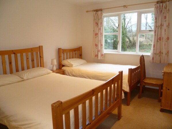 Quarto com duas camas de madeira, uma cadeira de madeira e uma escrivaninha.