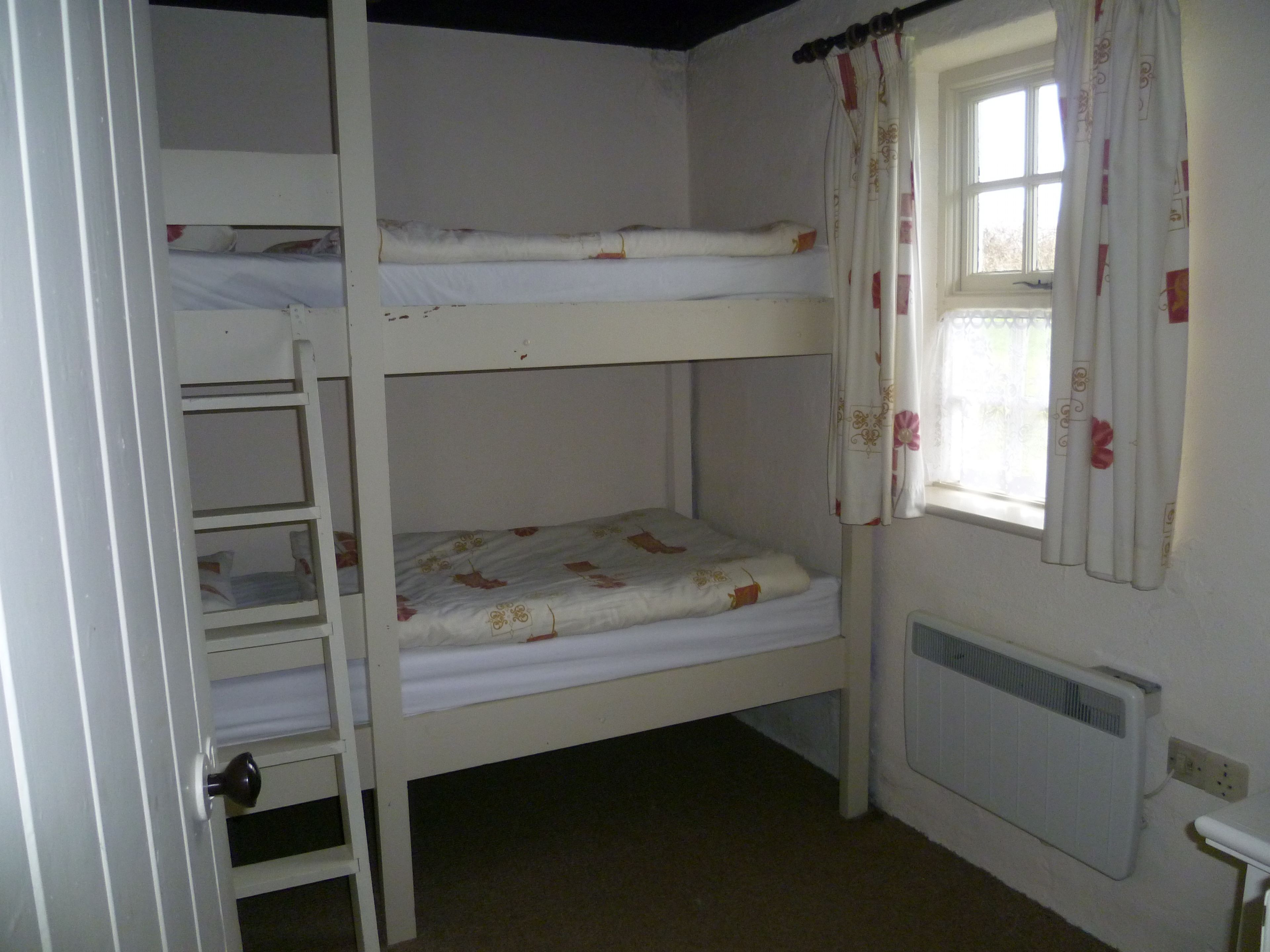 A bunk bed room with a window, radiator, and a door.