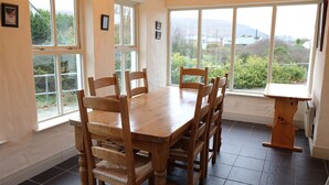 A dining area with a wooden table and chairs, large windows with a view of greenery and hills, and a small wooden side table. - Ballyvaughan Cottage No 14 (Ballyvaughan)