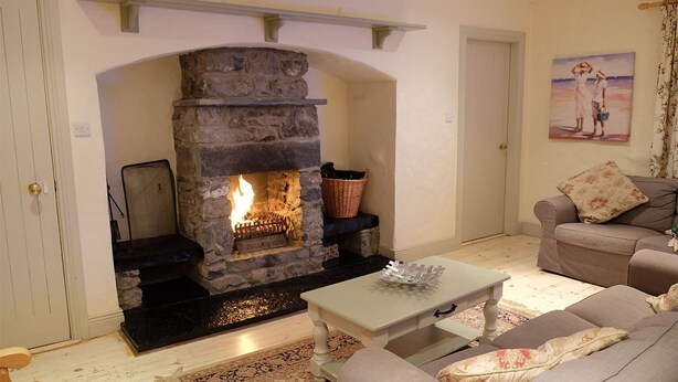 A cozy living room with a stone fireplace, a sofa, a coffee table, and a painting on the wall. - Ballyvaughan Cottage No 14 (Ballyvaughan)